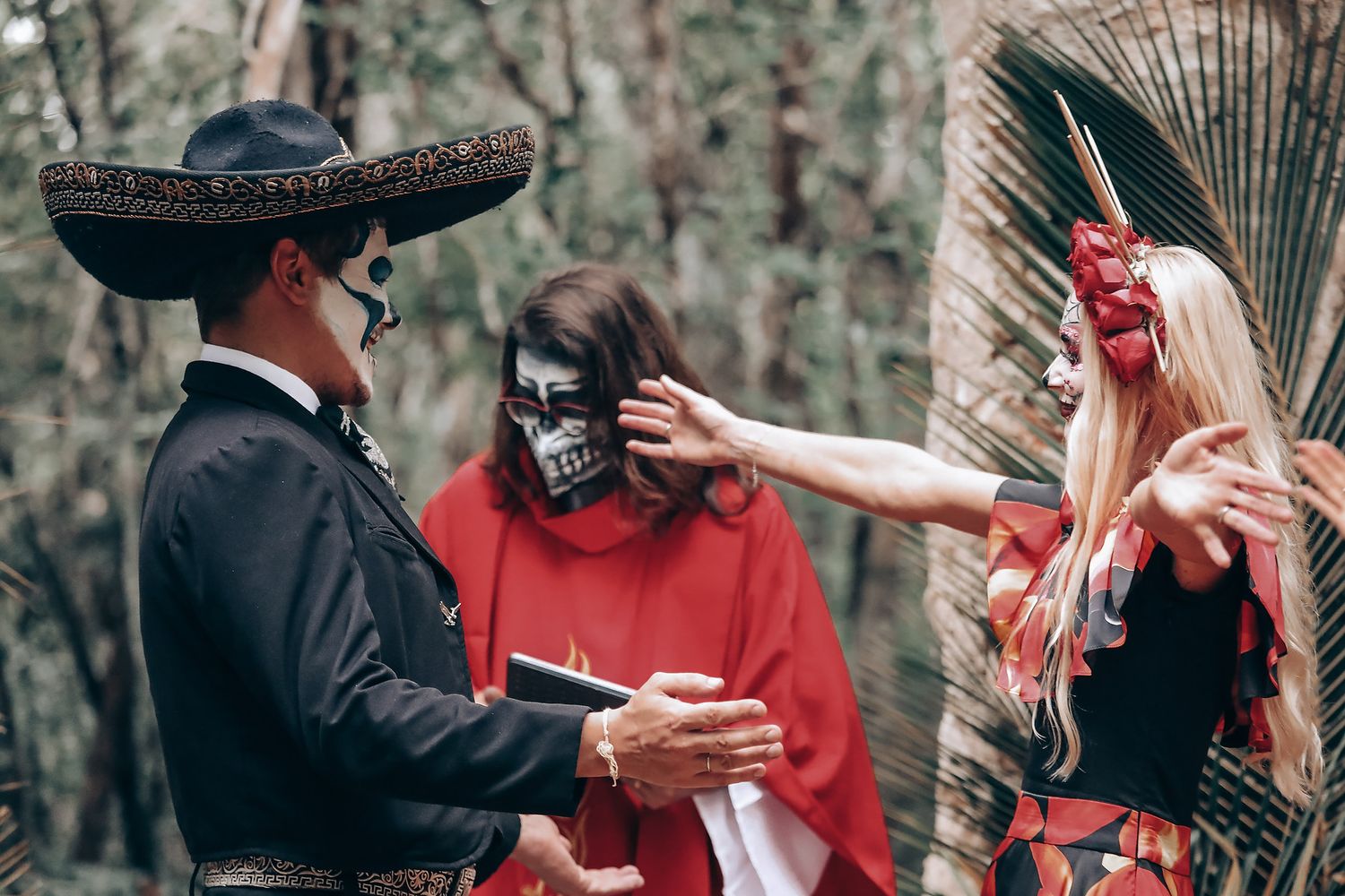 A couple in red and black outfits pose dramatically in a wooded setting with stone walls.