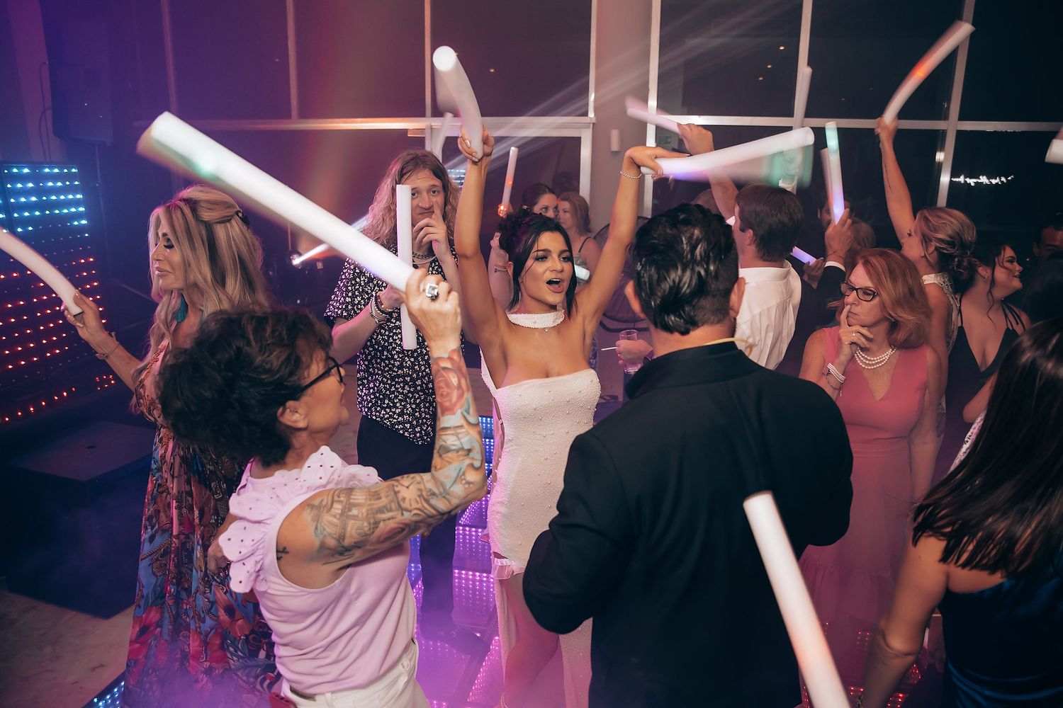 Party guests dance with light-up foam sticks on a colorfully lit dance floor.