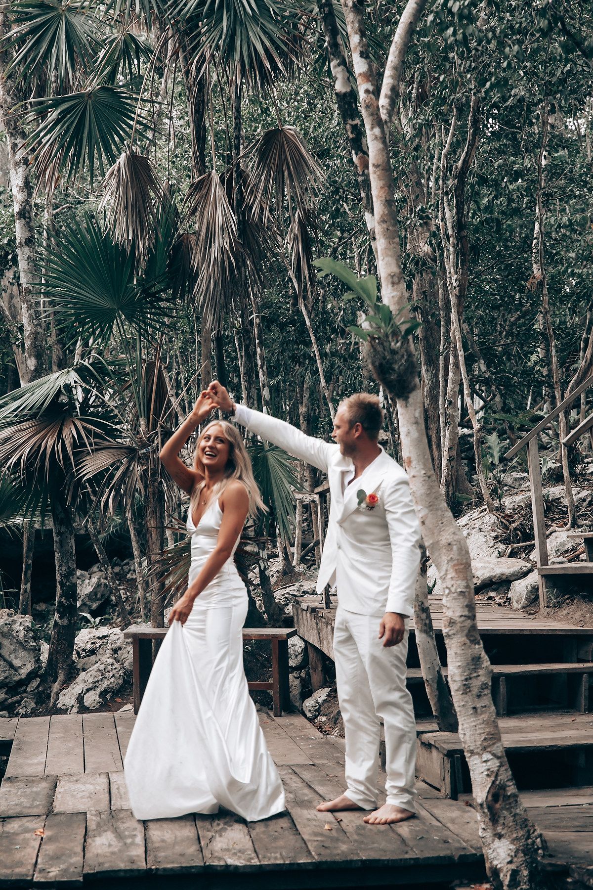 Couple dancing together on wooden deck surrounded by palm trees and tropical foliage.