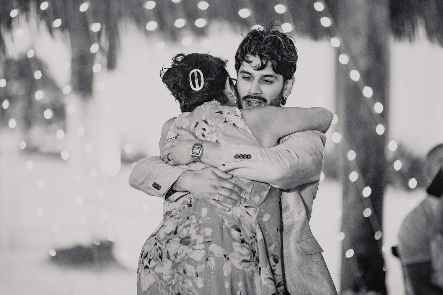 Black and white photo of a man and woman sharing a warm embrace at a festive event with bokeh lights.