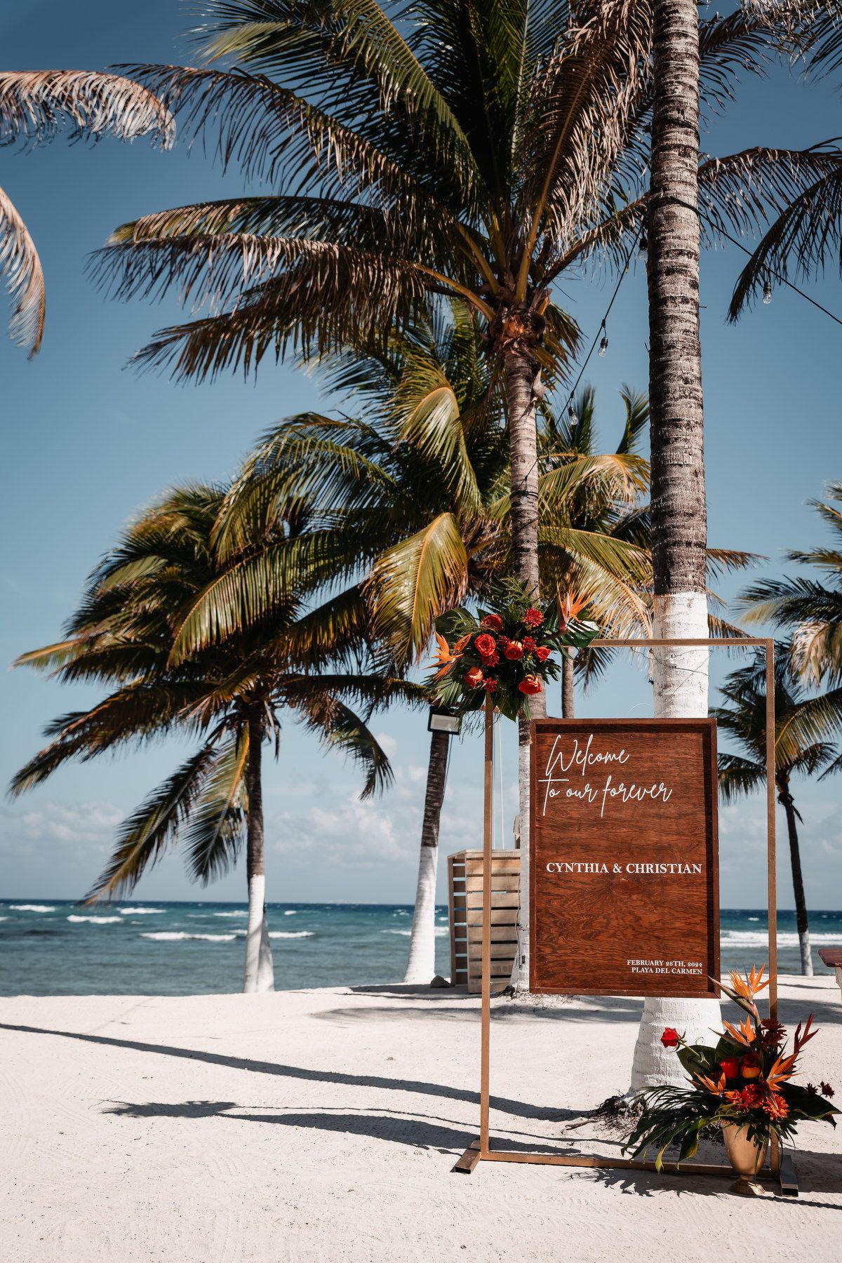 Tropical beach wedding welcome sign for Cynthia and Christian surrounded by palm trees on white sand.