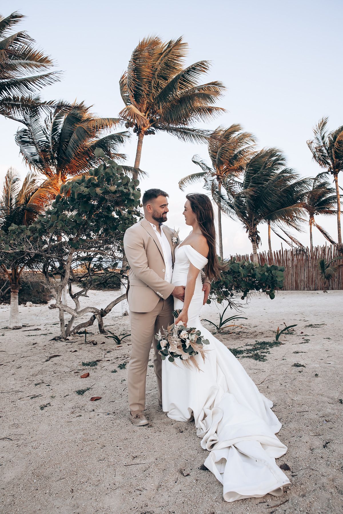 A romantic beach wedding scene with swaying palm trees as newlyweds dance in the sand at sunset.