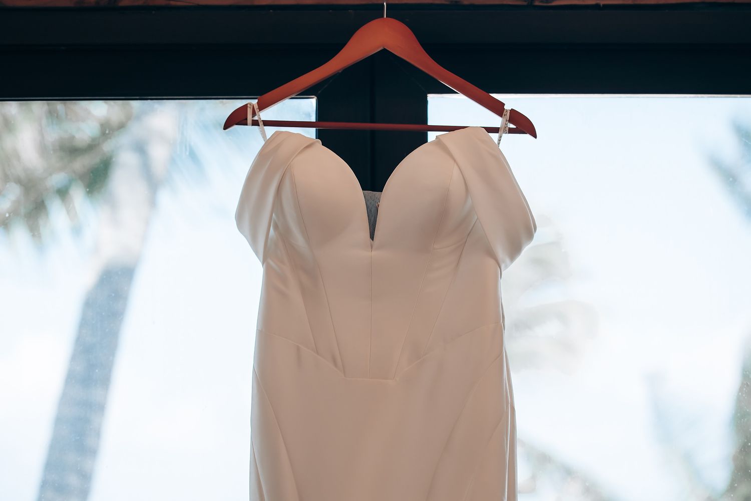 A beige sleeveless dress with a v-neck neckline hangs on a wooden hanger against a light background.