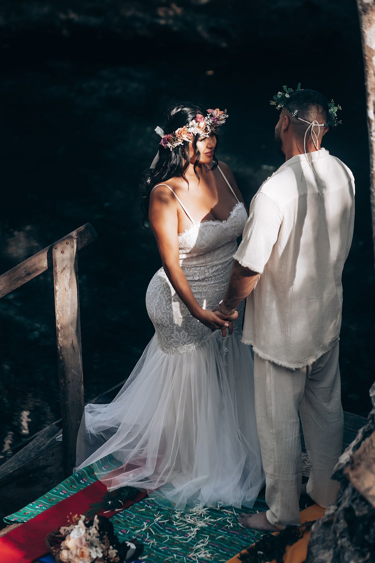 Couple in wedding attire dancing intimately in a dimly lit setting with decorative lighting.