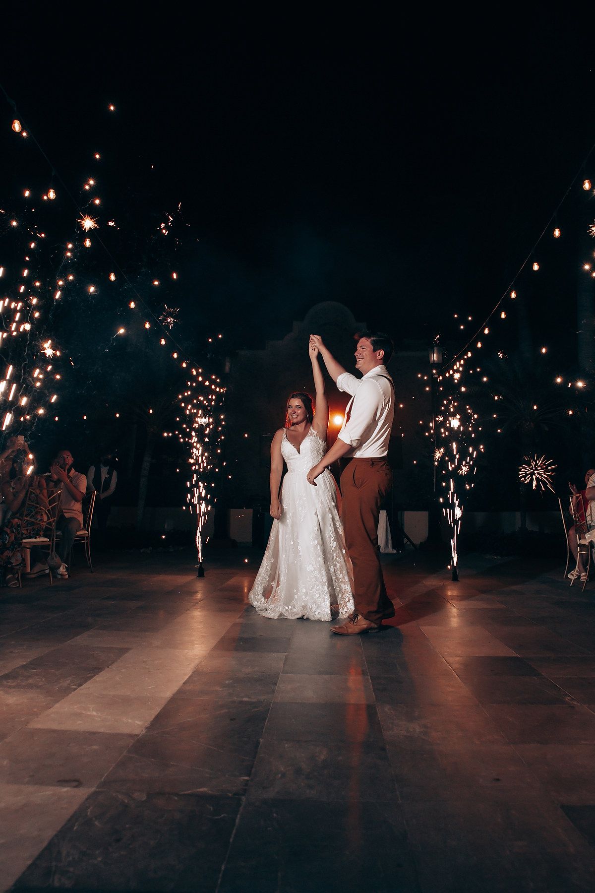 Wedding couple dances under sparklers creating magical light trails in a dark reception venue.