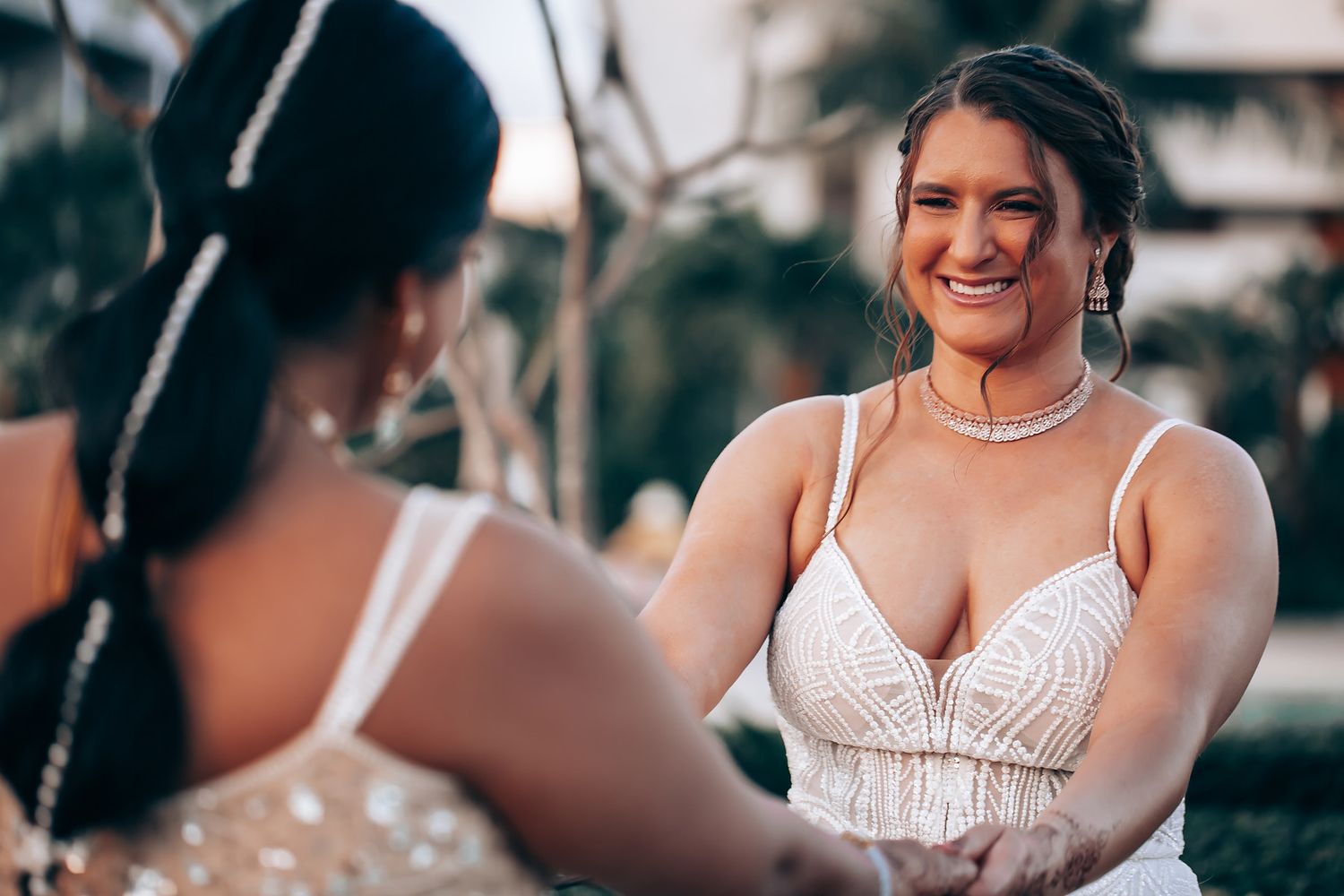 A candid moment captured between two people in white wedding dresses outdoors.