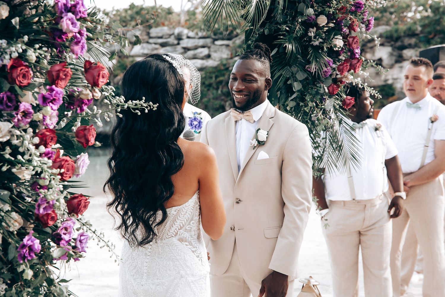 Wedding party in coordinated beige and white outfits under floral decorations.