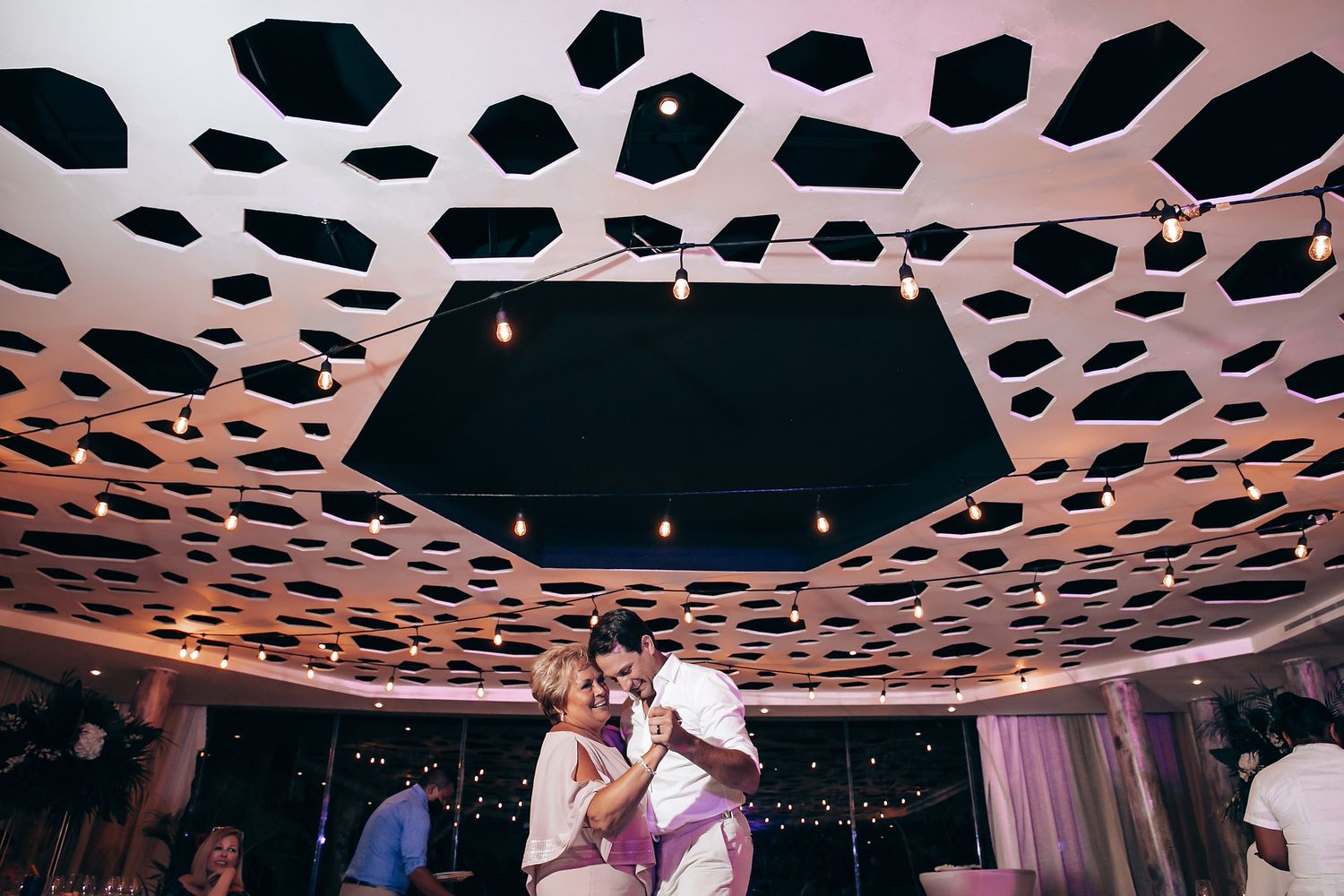 Modern reception venue with geometric patterned ceiling and ambient lighting.