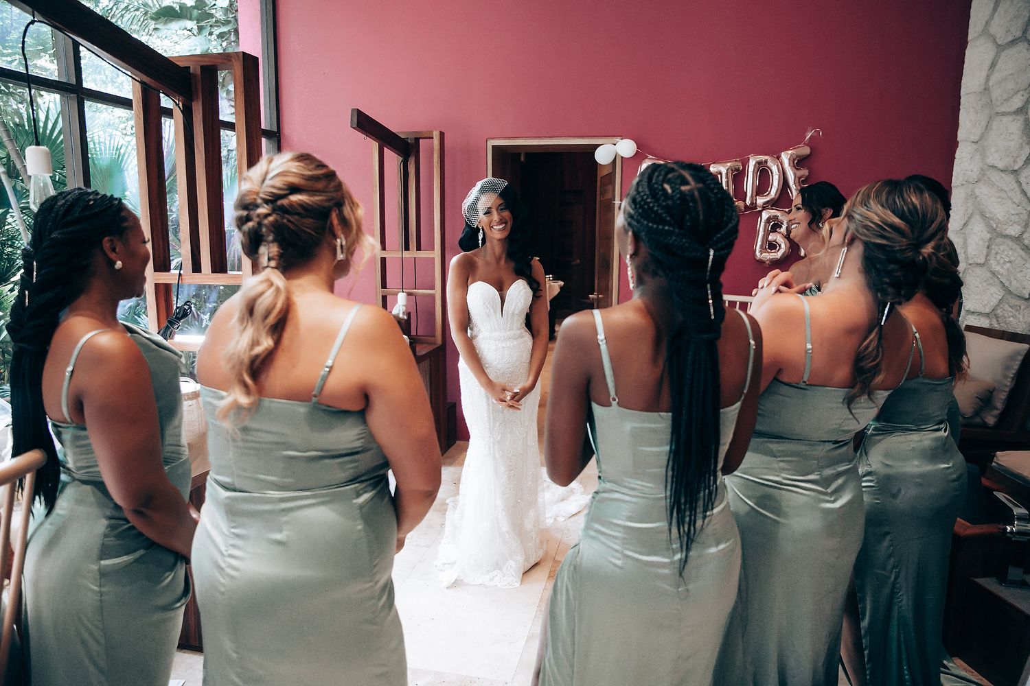 Bridesmaids in sage green dresses gather around a bride wearing a white wedding gown.