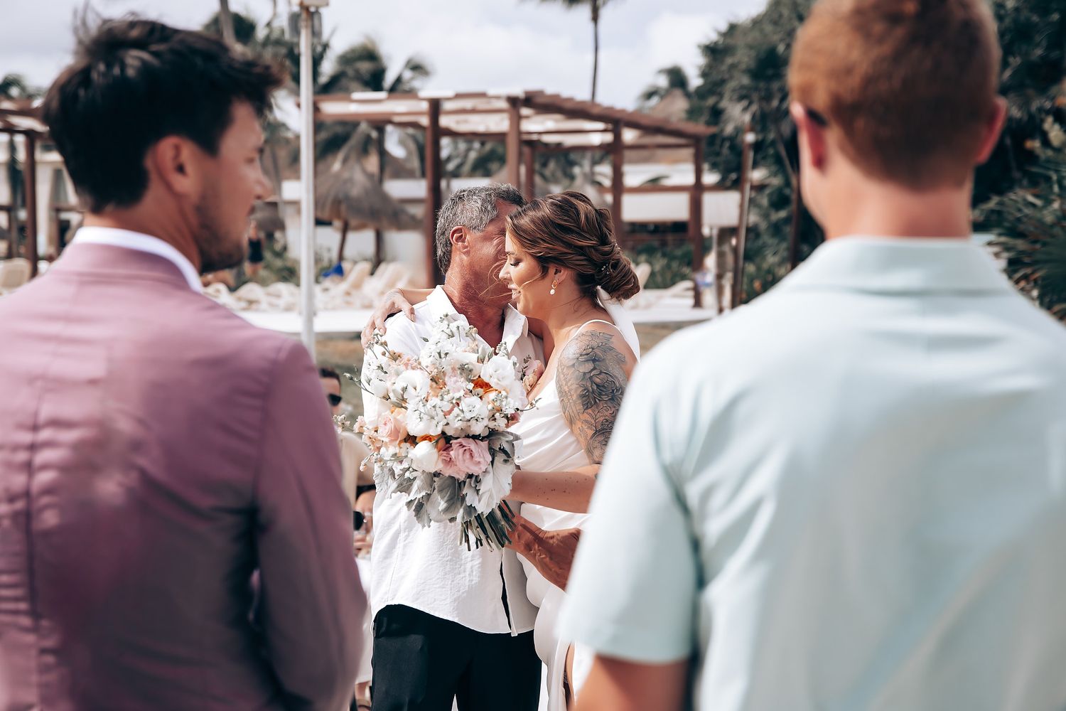 Wedding party in neutral colors poses together at a tropical beach venue during sunset celebration.