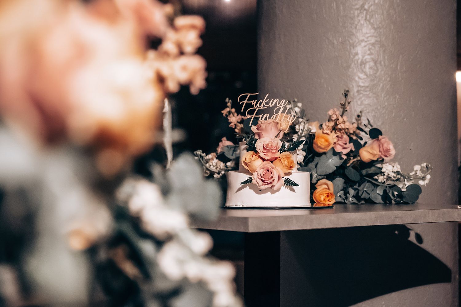 Elegant wedding cake display with peach and coral flowers surrounded by romantic candlelight and floral arrangements.