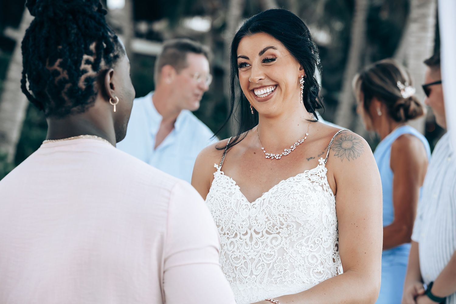 The image shows a bride and groom embracing and smiling at each other during their wedding ceremony on a beach.