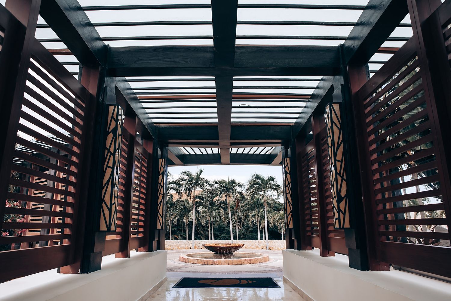 A covered walkway with wooden slats and palm trees visible in the background.