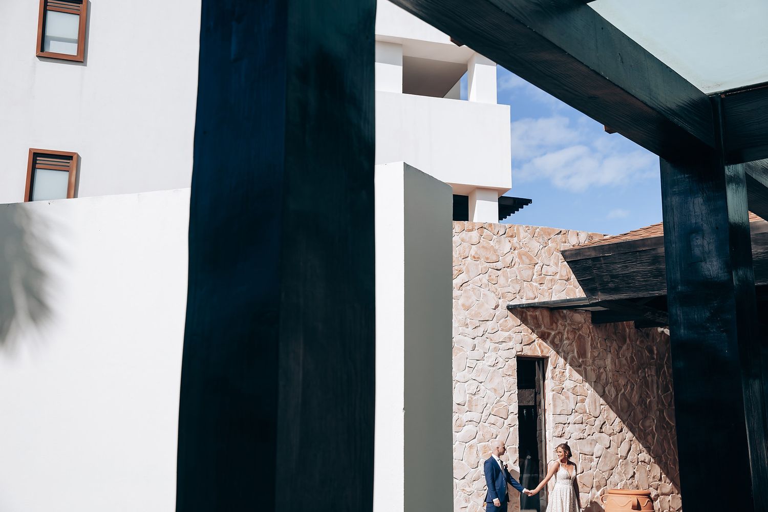 A person walks through an archway in a building with white walls and blue sky visible.