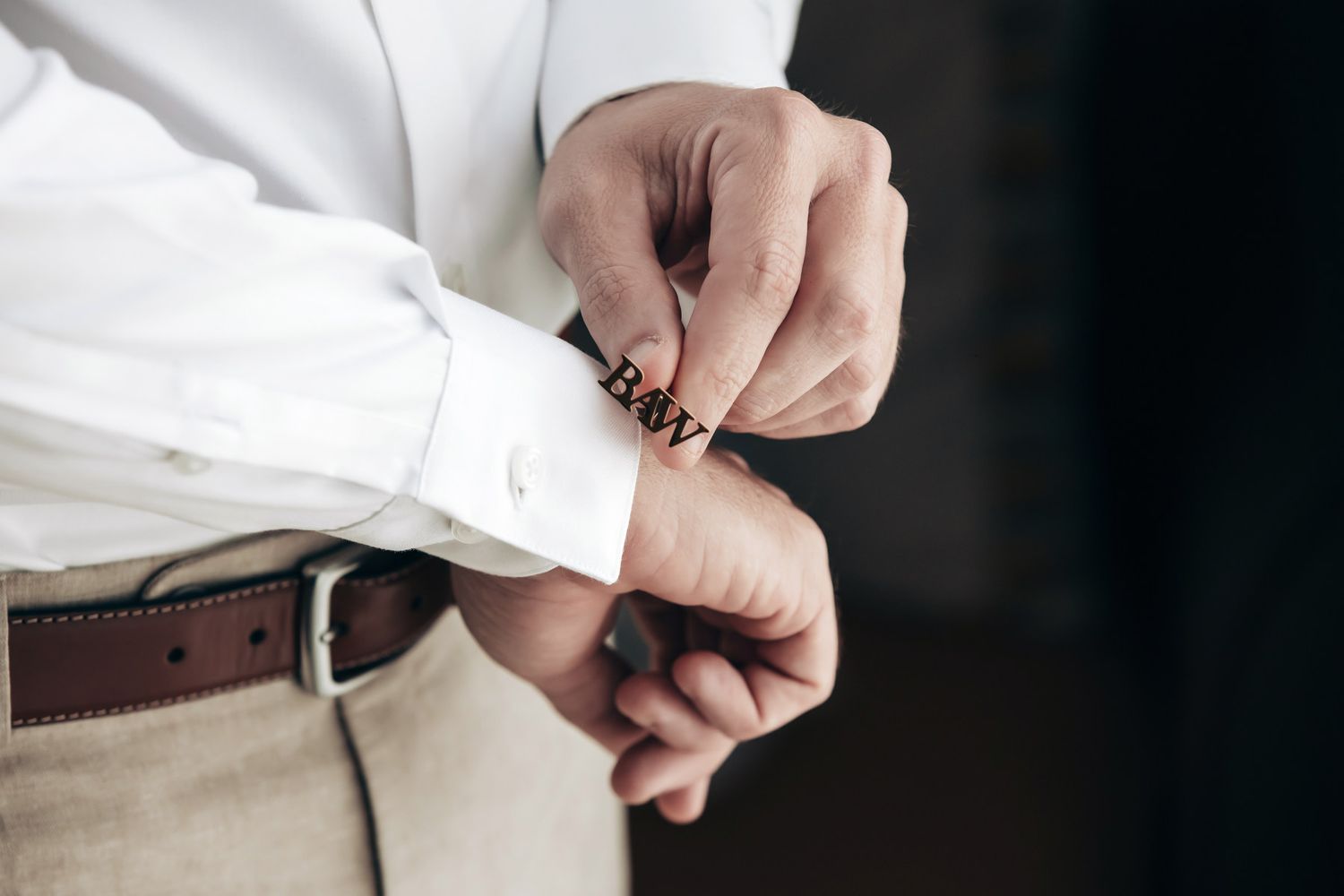Groom fastening personalized cufflinks on white dress shirt sleeve on wedding day.