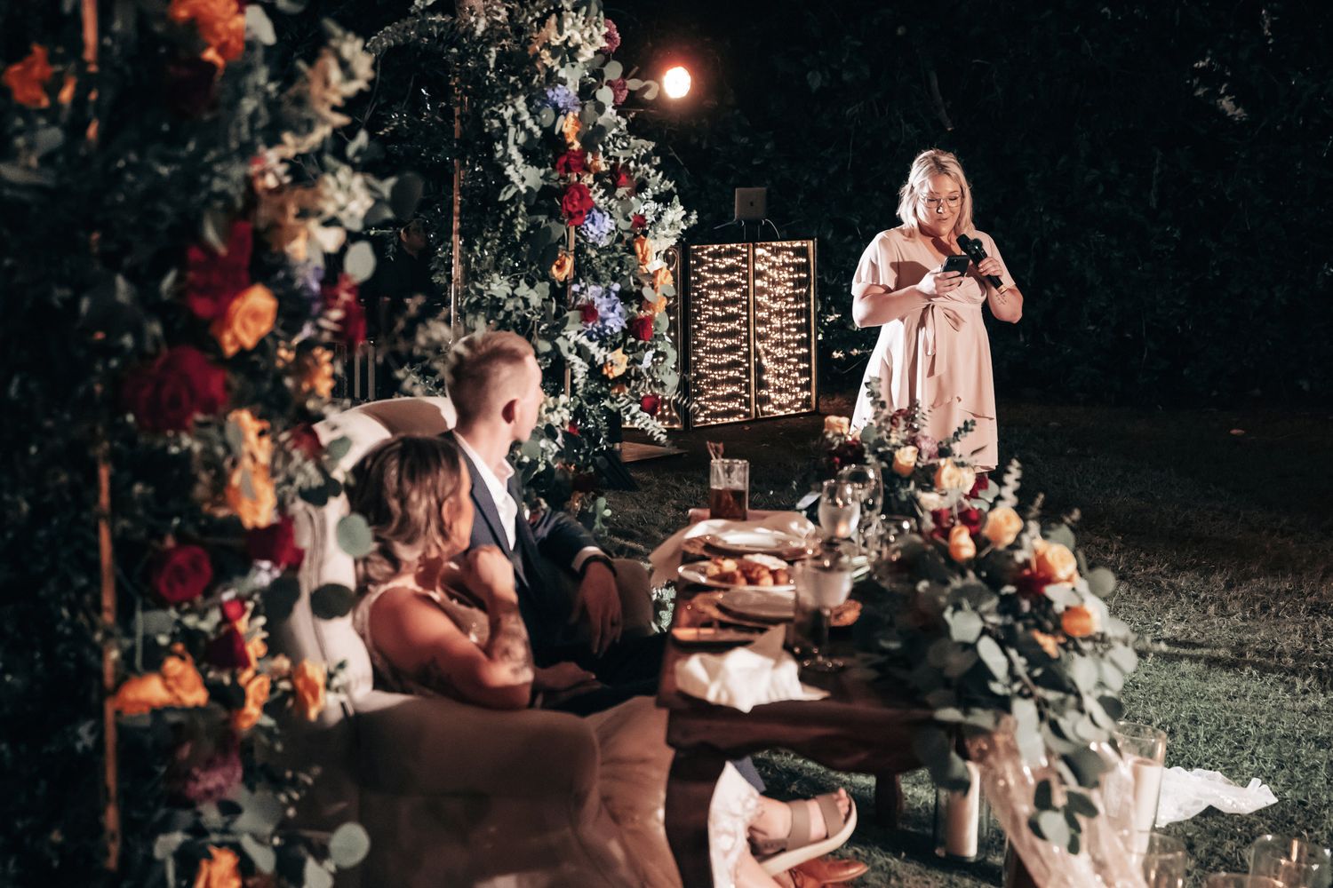Wedding guest gives a heartfelt speech at a beautifully decorated nighttime outdoor reception table.