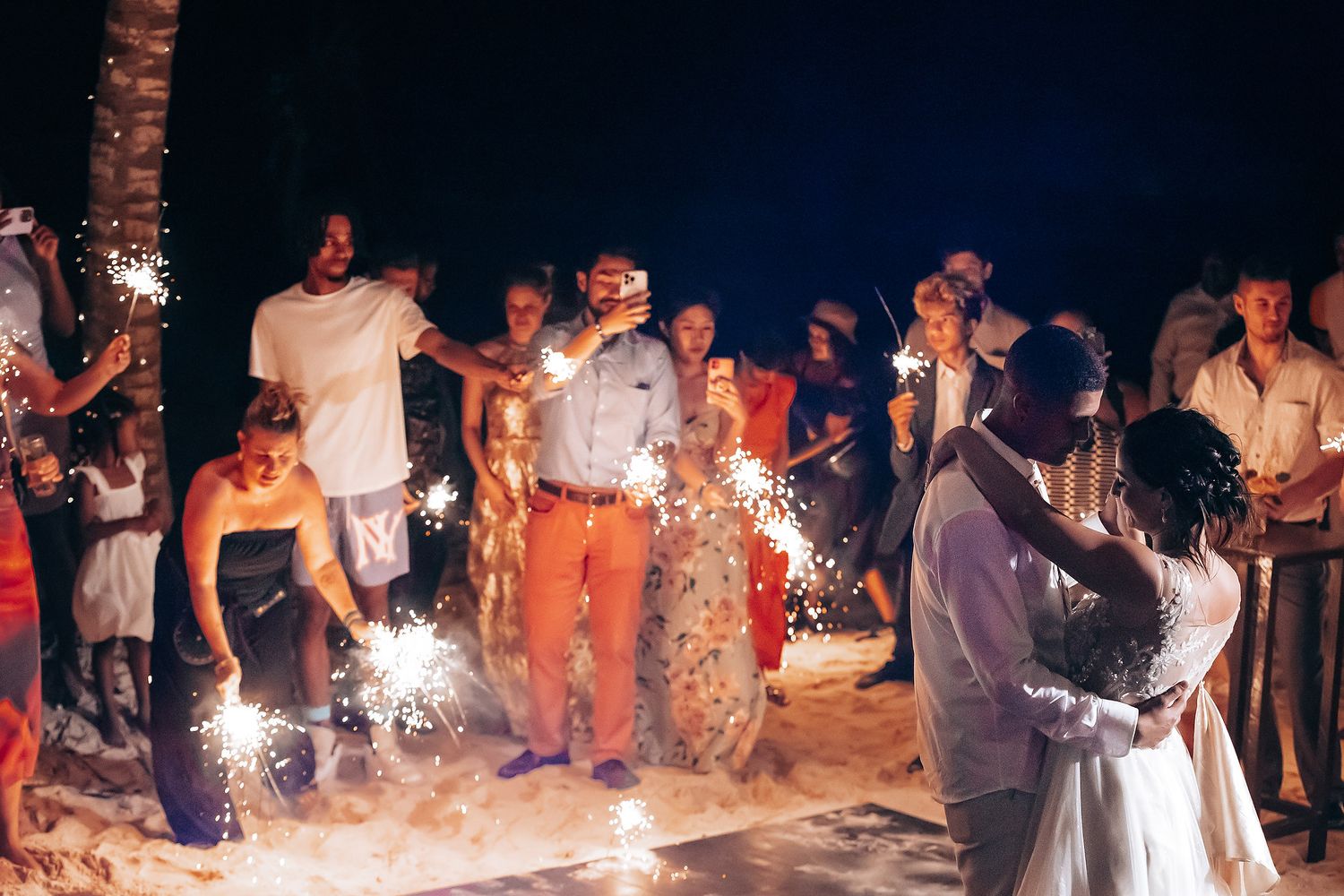 Wedding celebration at night with sparklers creating a magical atmosphere on the beach.