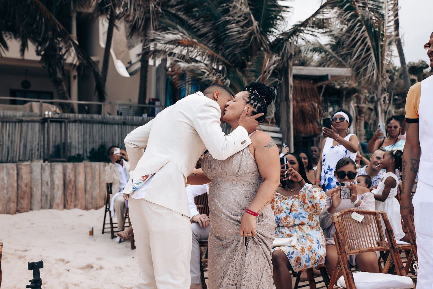 Wedding celebration on a tropical beach with palm trees and guests in light colored attire.