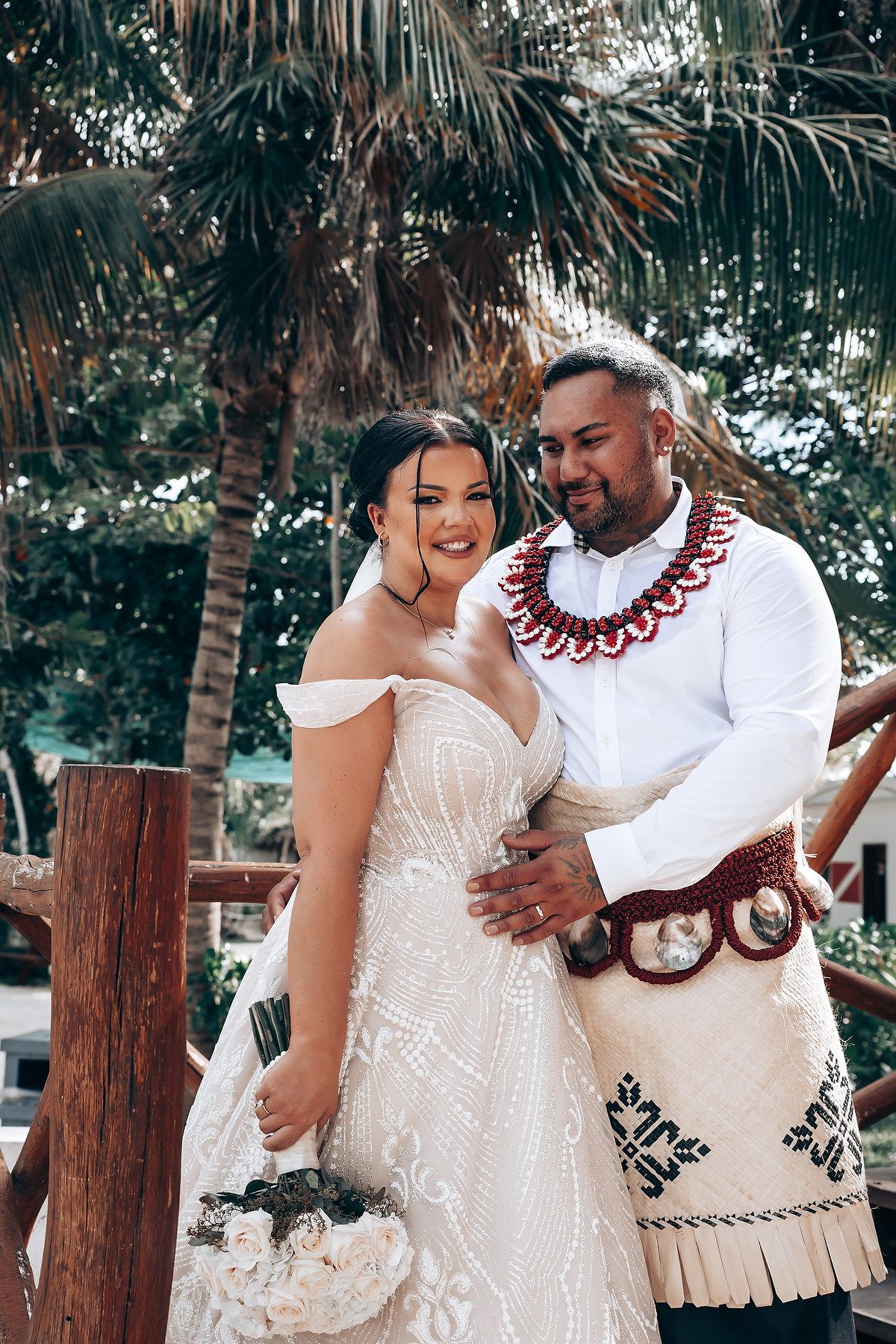 Couple in traditional wedding attire share intimate moments in a tropical garden setting with palm trees.