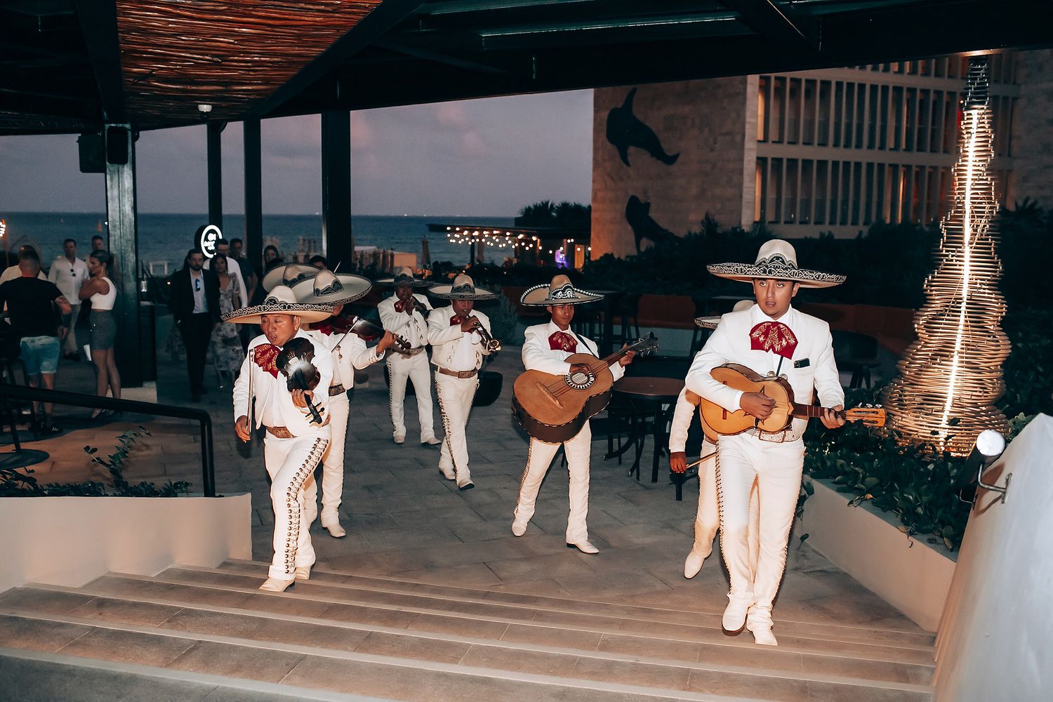 Musicians perform on stage at an outdoor venue with string lights creating a warm ambiance.