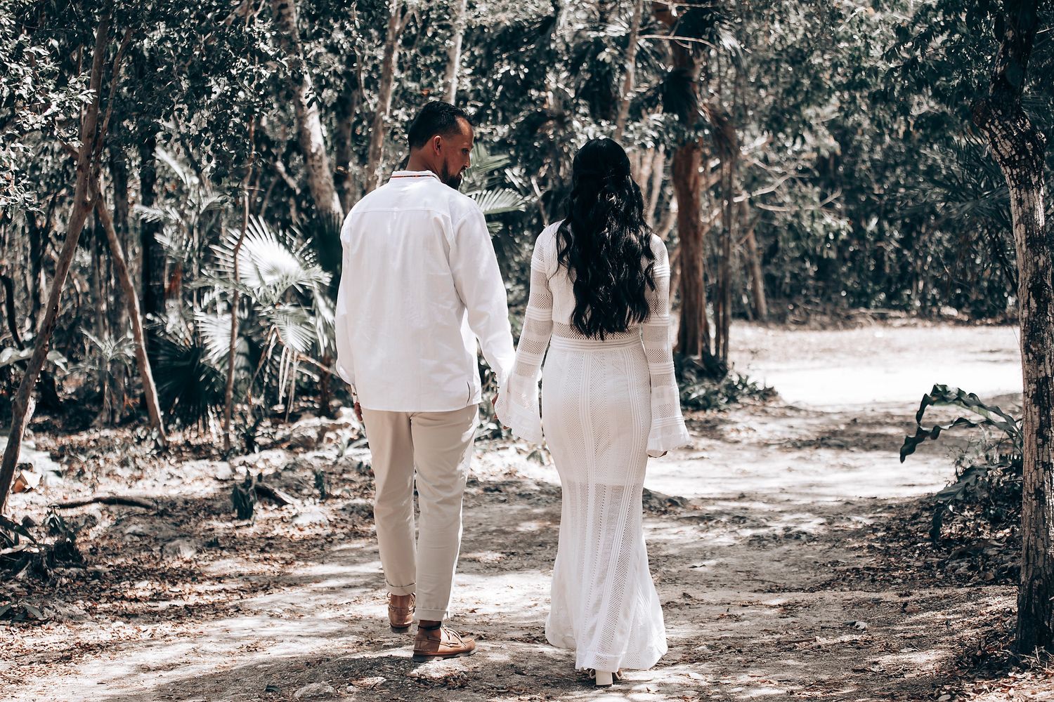 People in white clothing walking through a wooded area during a ceremonial gathering.