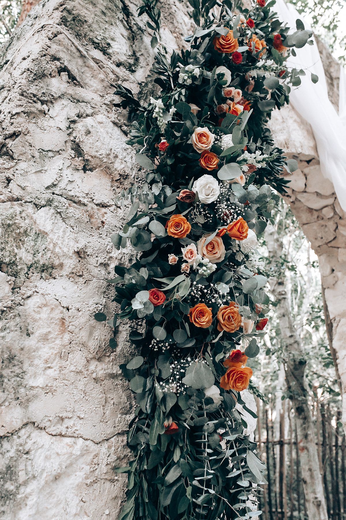 Stone archway decorated with orange roses and greenery for an outdoor wedding ceremony.