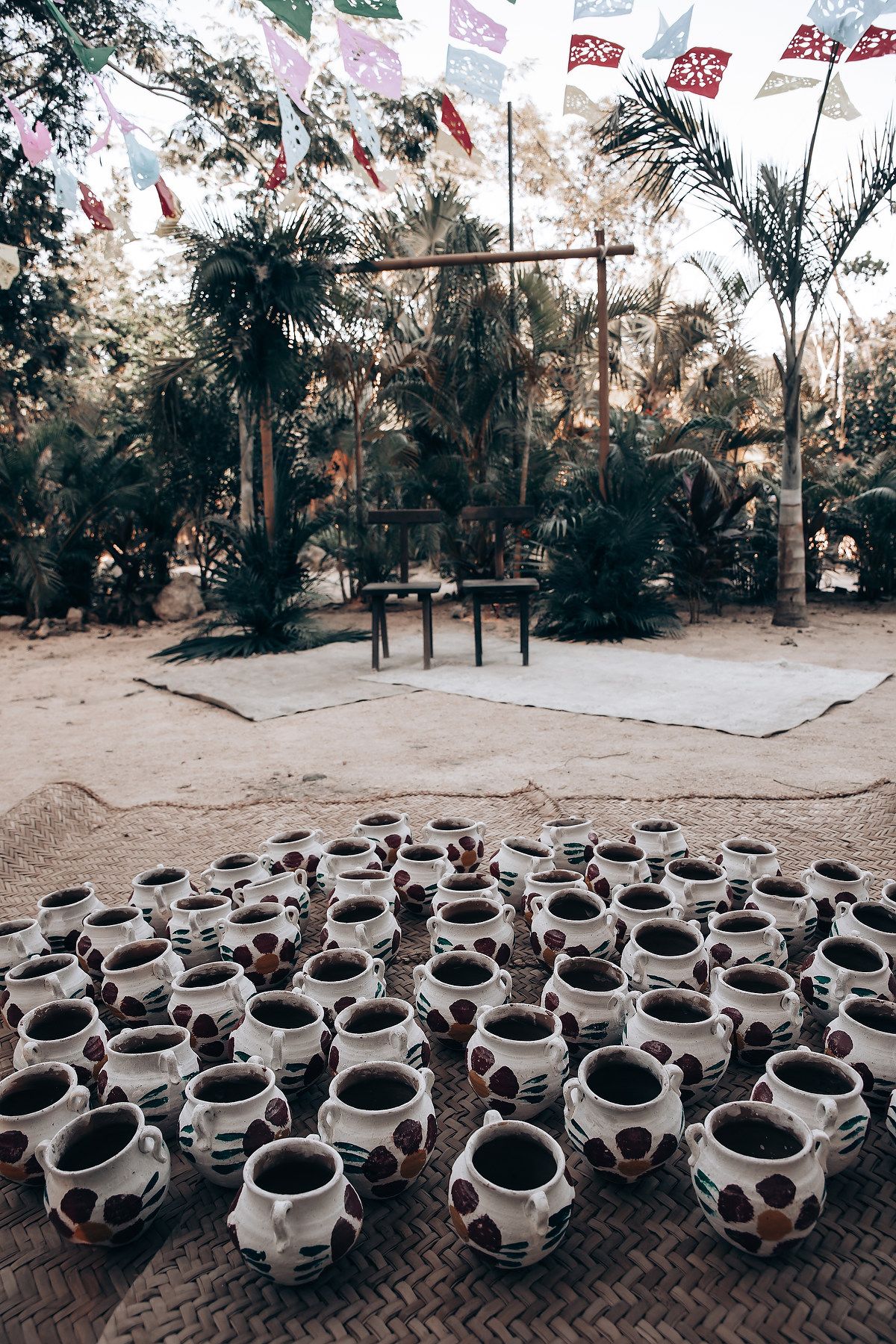 Rows of decorative clay pots with polka dot patterns arranged outdoors under palm trees and festive bunting.