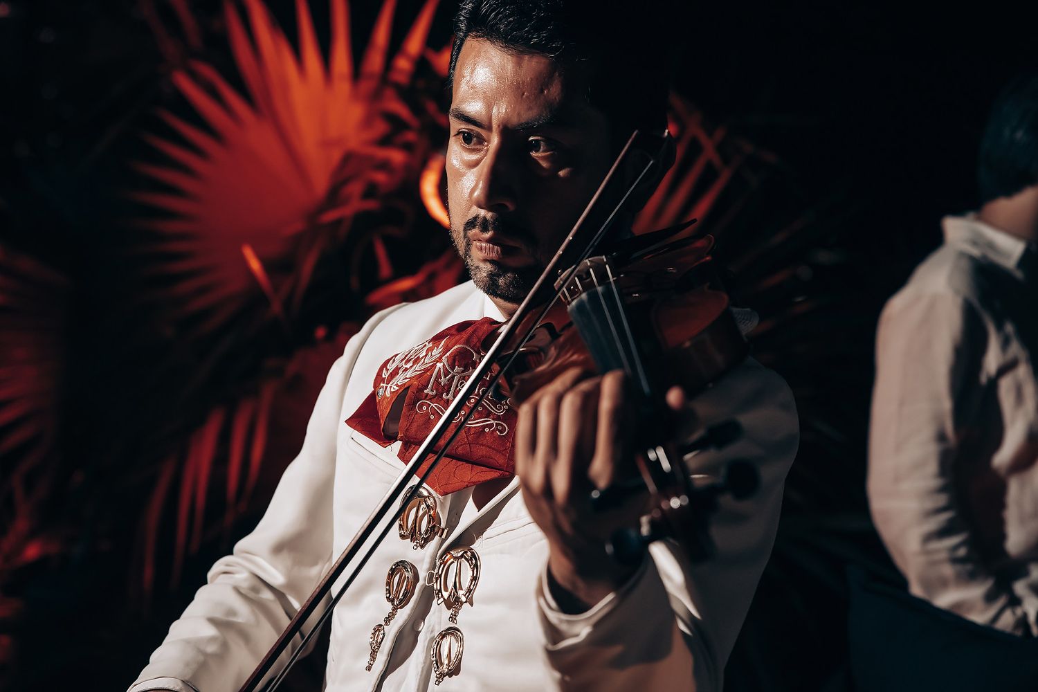 Violinist performing at an evening event with dramatic red lighting.