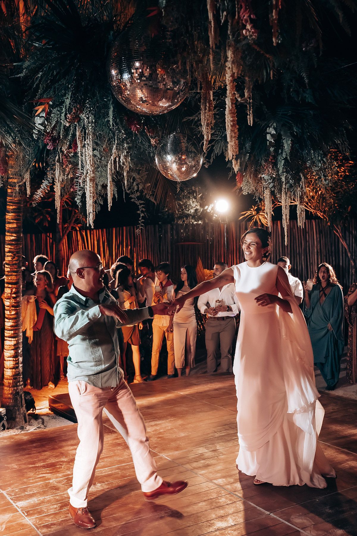 Wedding couple shares a romantic dance on a wooden dance floor surrounded by trees and string lights.