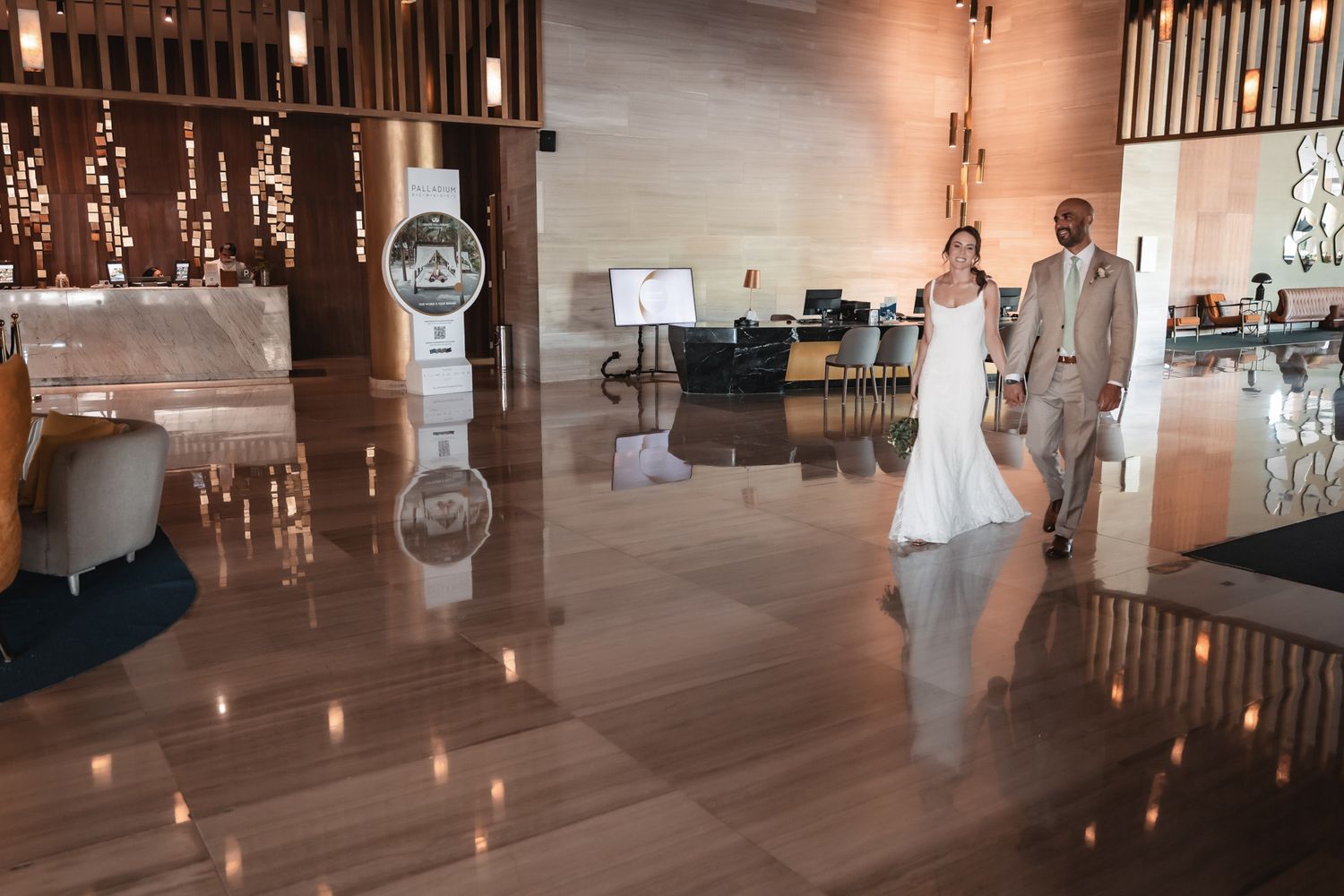 Bride and groom walking through modern hotel lobby with reflective floors on their wedding day.