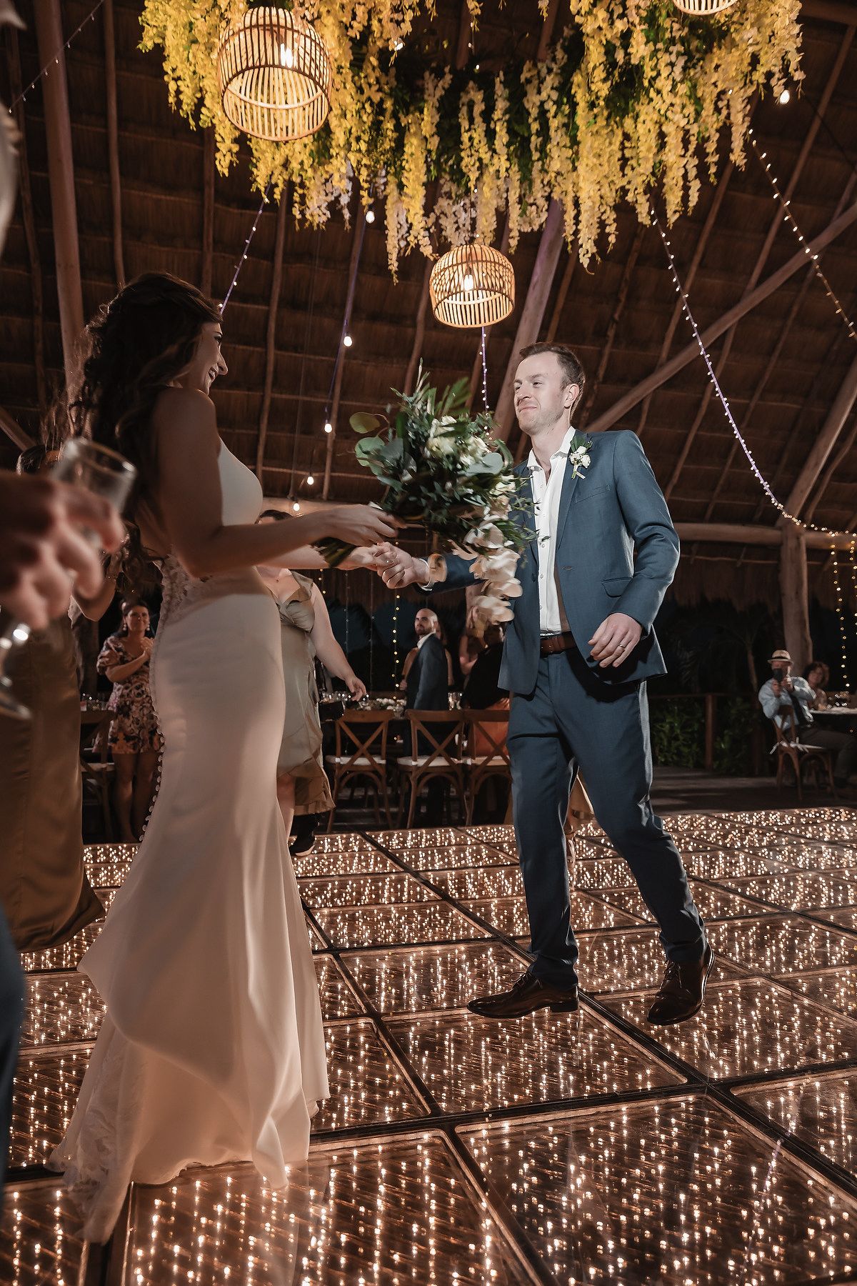 Bride and groom share first dance on sparkling LED dance floor under hanging greenery and chandeliers at elegant wedding reception.