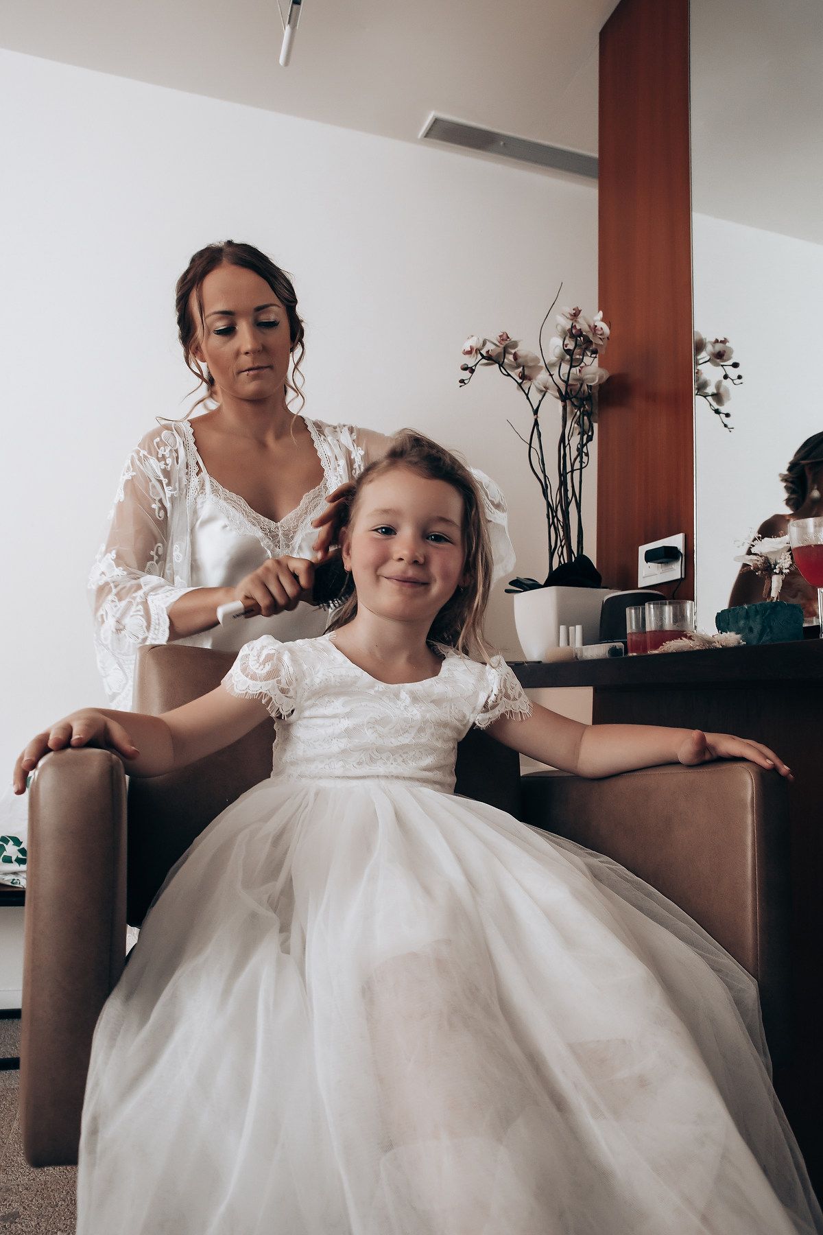 Young girl in white dress being prepared for a special occasion in an indoor setting.