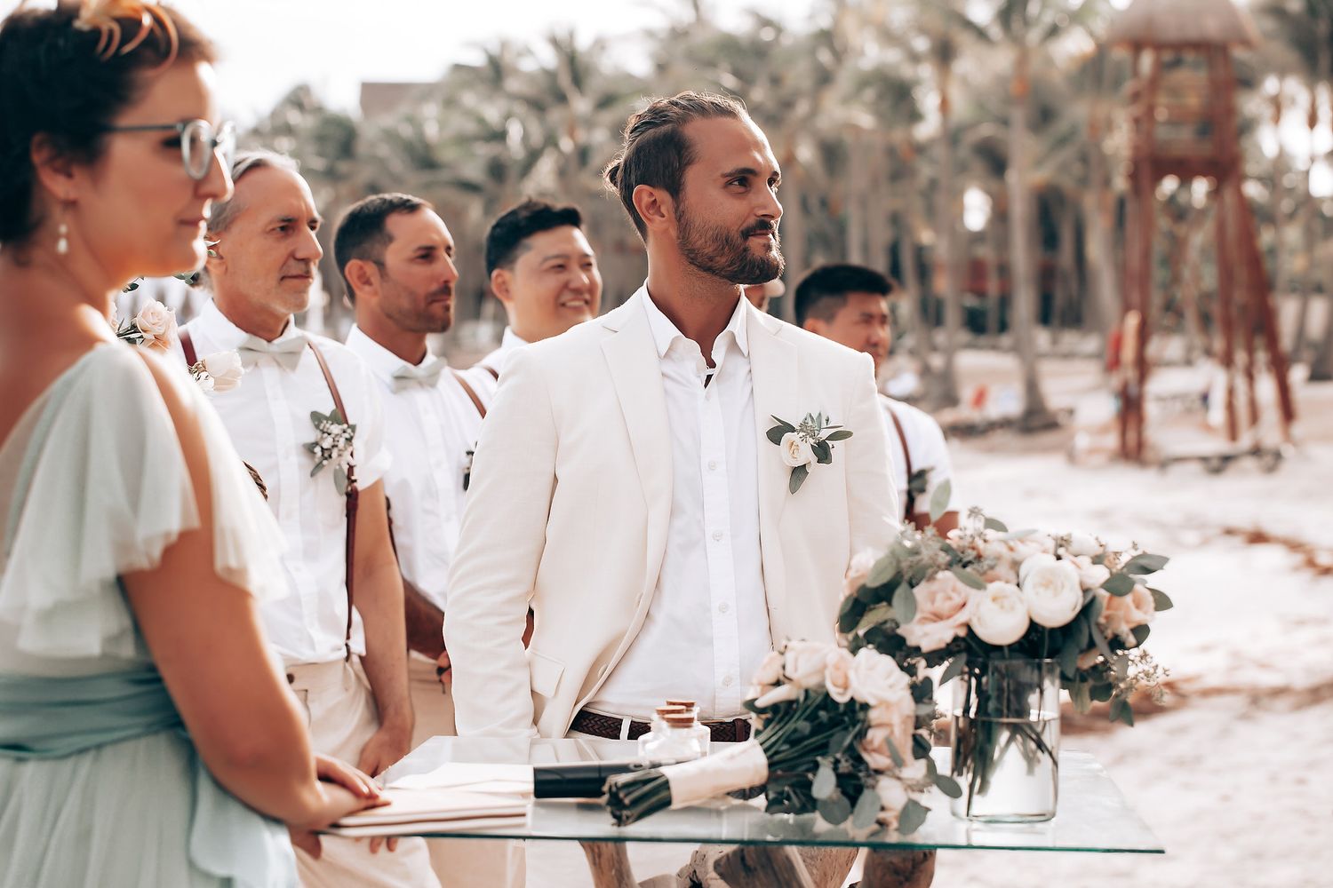 A beachside wedding ceremony setup with white floral arrangements and palm trees in the background.