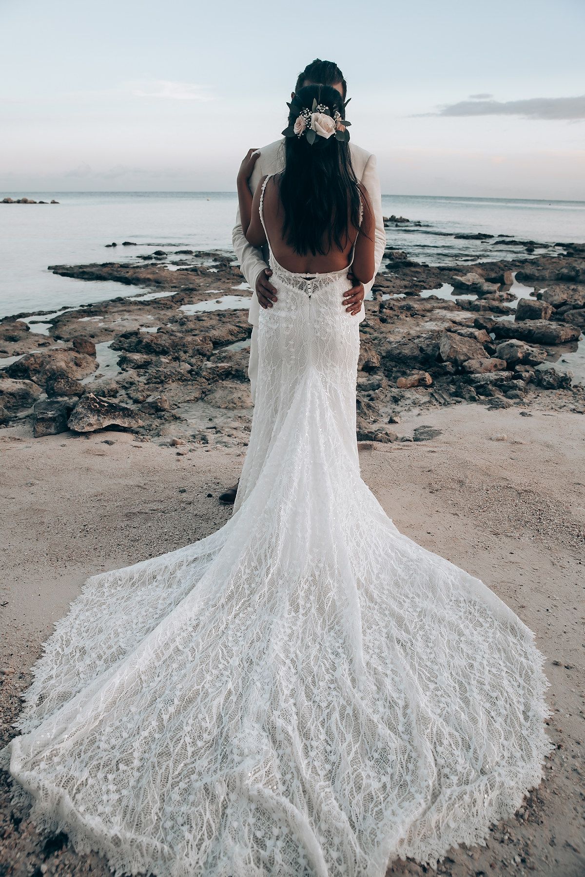 A detailed view of a lace wedding dress train spread out on rocky beach terrain.