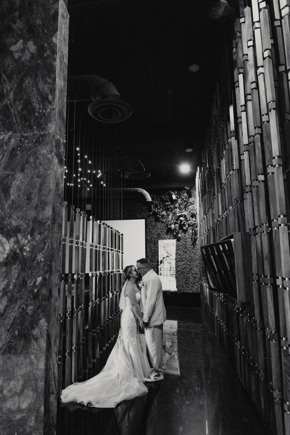 Bride and groom share romantic kiss in elegant corridor in black and white wedding portrait.