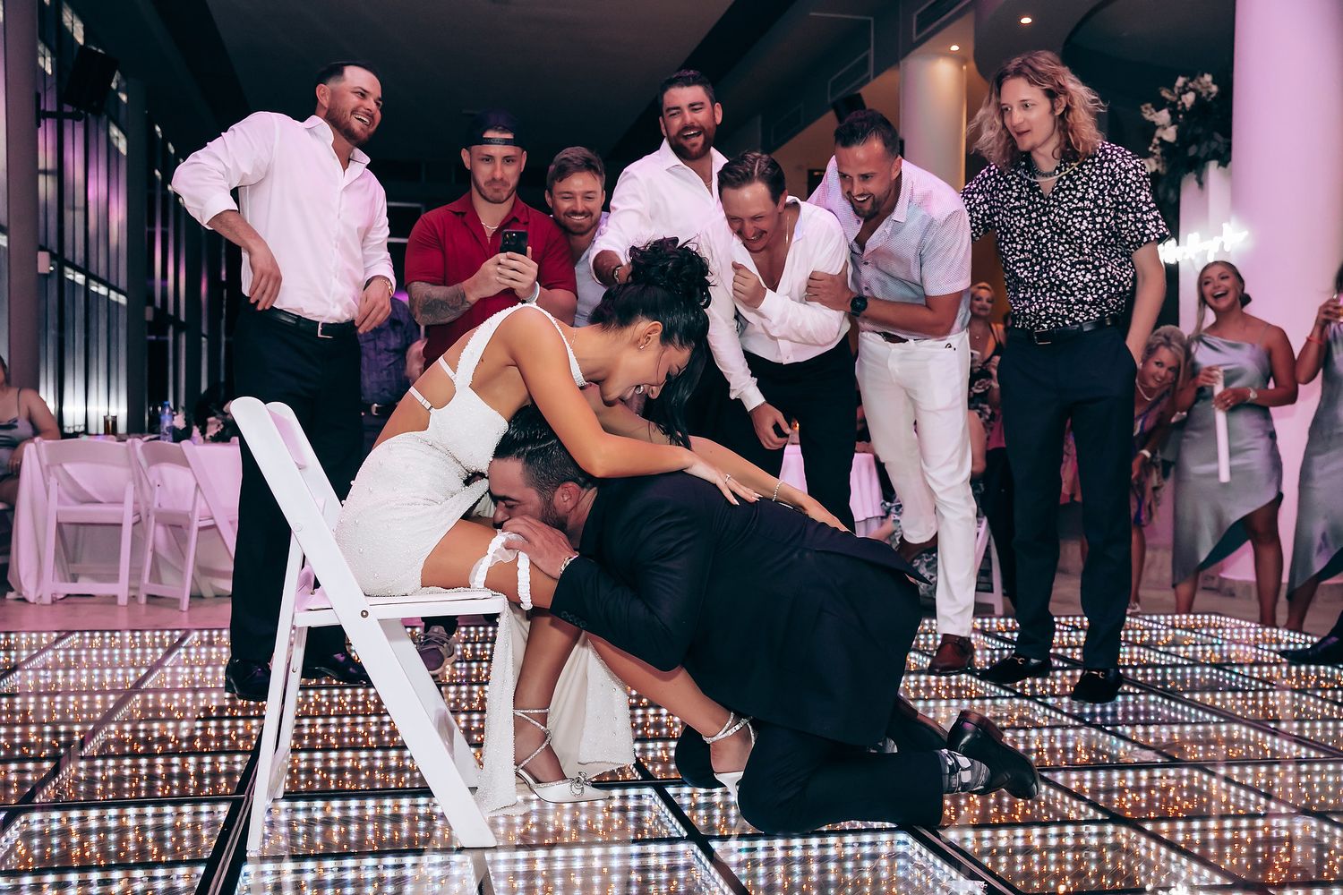Wedding guests perform a limbo dance game on an illuminated dance floor.