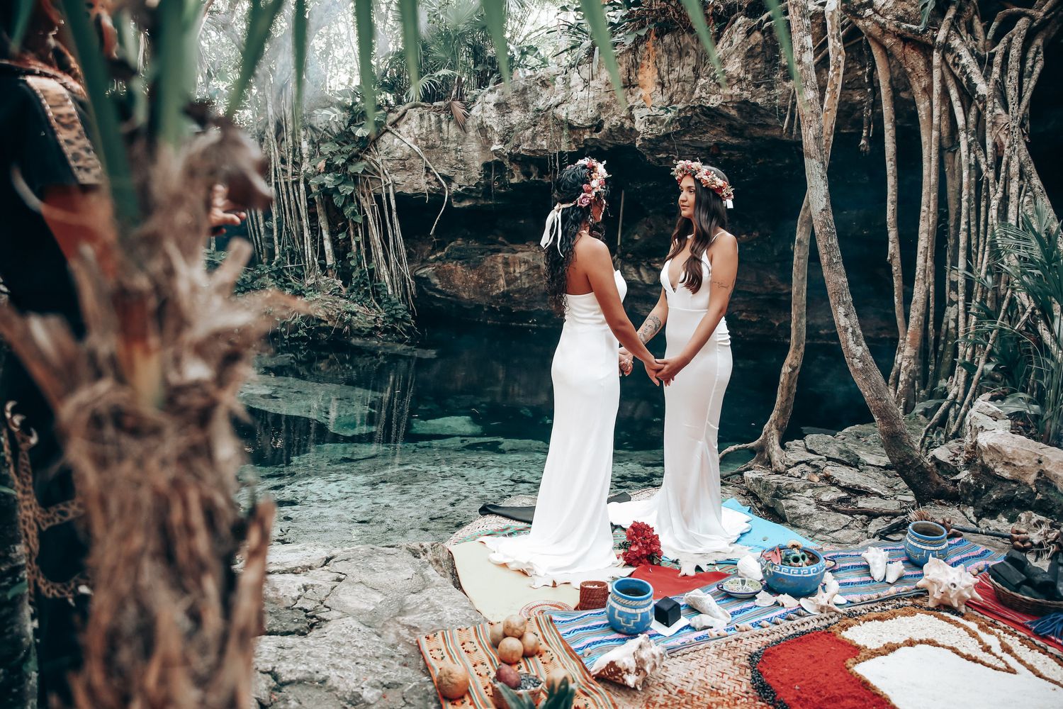 A wedding ceremony takes place in a lush outdoor forest setting with white decor and floral arrangements.