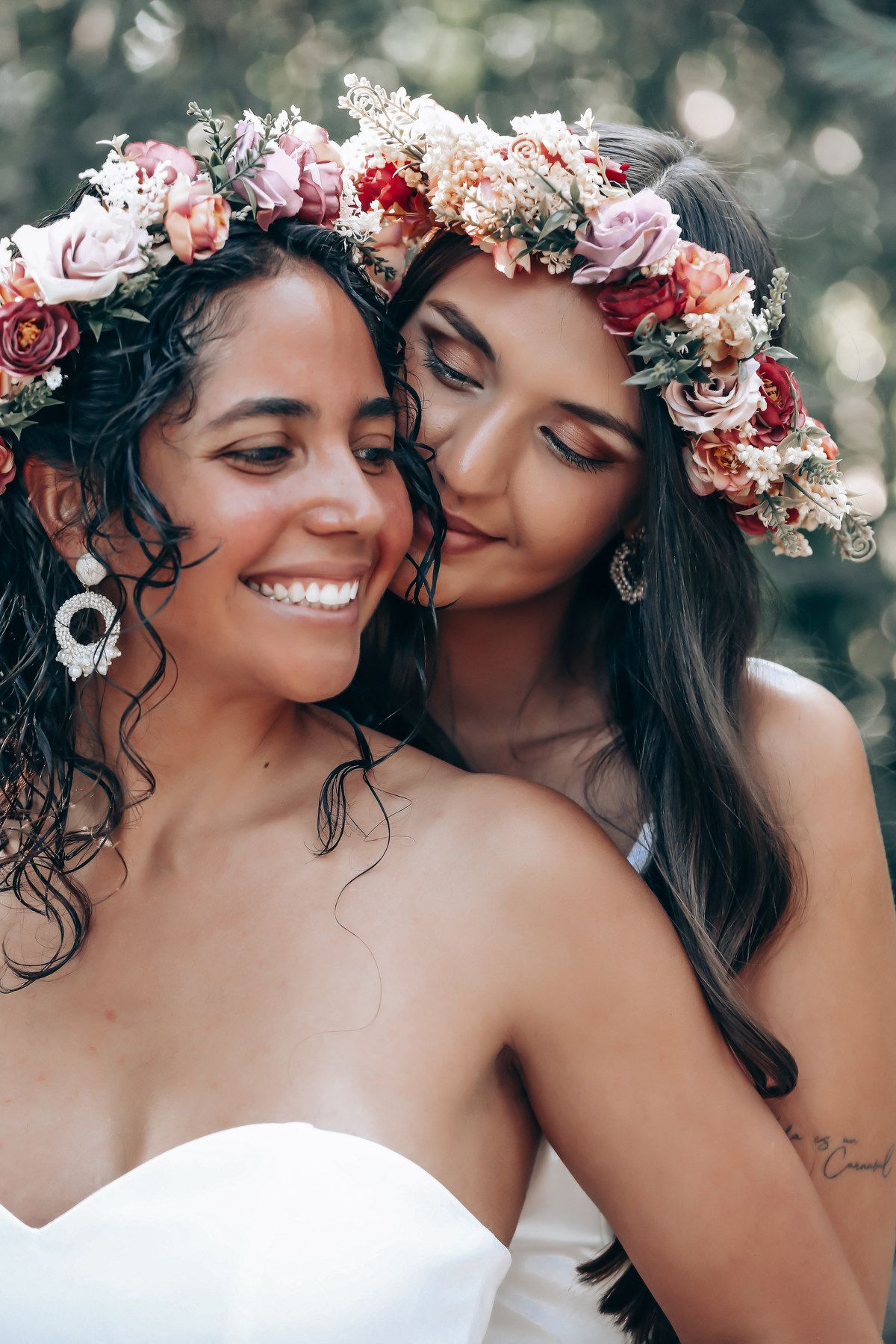 Two brides wearing floral crowns share joyful moments during their forest wedding photoshoot.