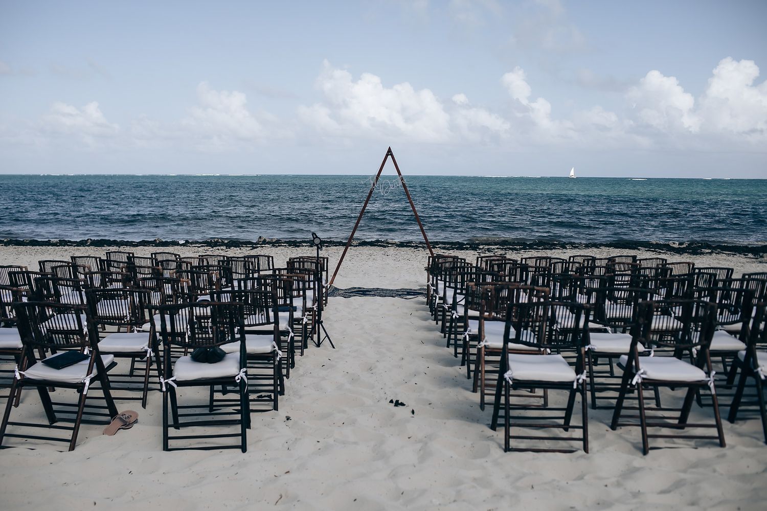 Black beach chairs arranged in rows for an oceanfront wedding ceremony.