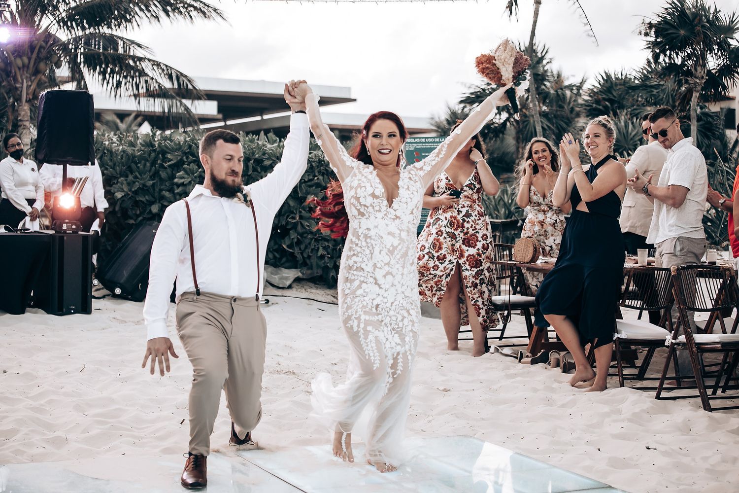 Beach wedding celebration with guests cheering as couple walks down aisle.