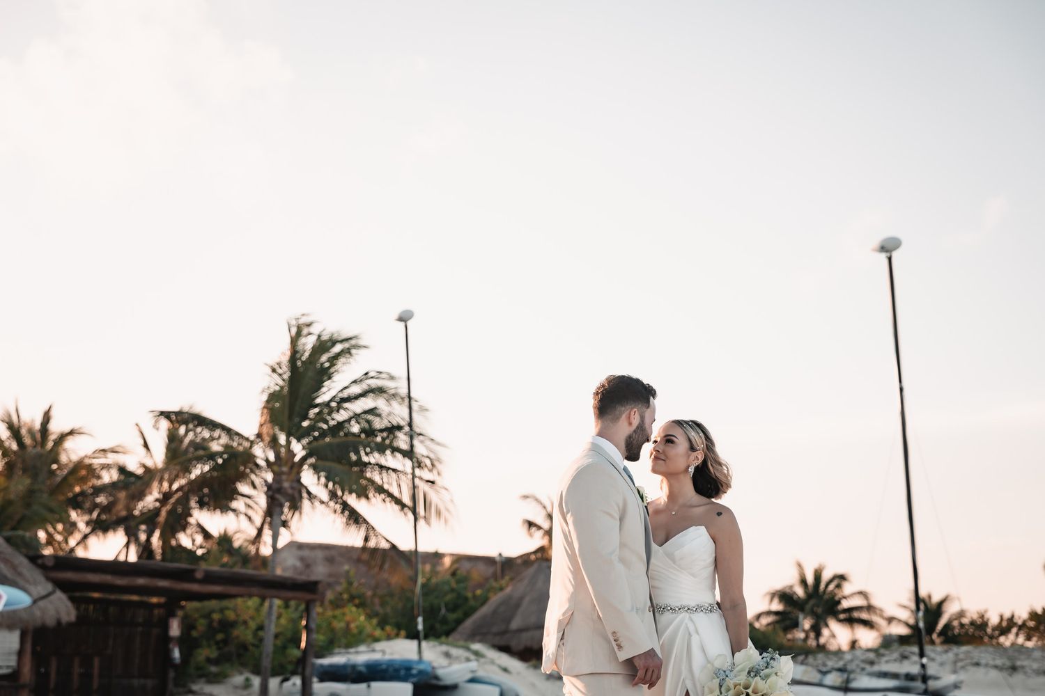 Bride and groom holding hands at sunset with tropical palm trees at beach wedding venue.
