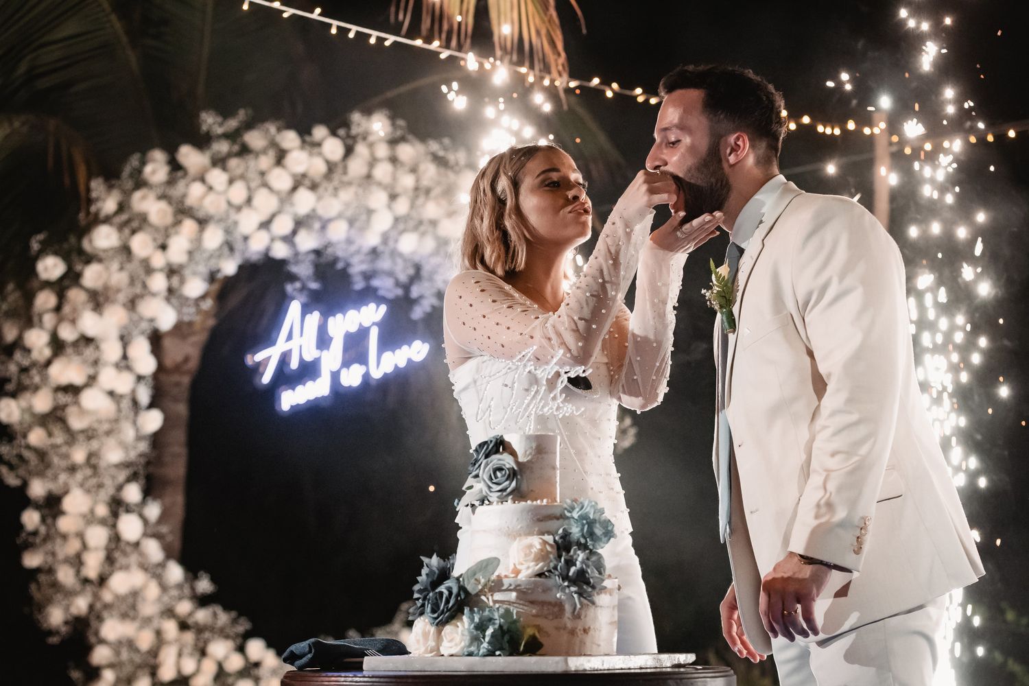 Bride and groom cut their wedding cake surrounded by sparkling fireworks and a neon love sign.