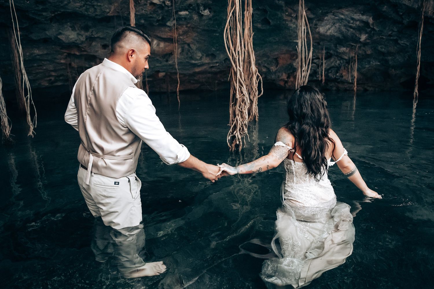 A couple wades through crystal clear cenote waters during their photo session.