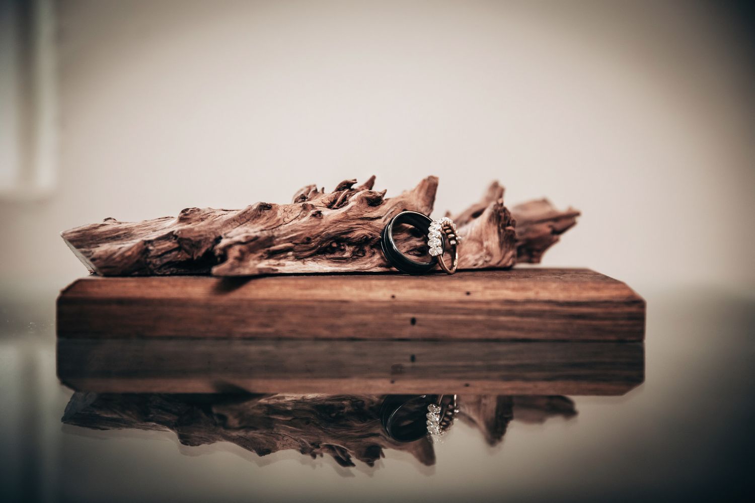 A wedding ring resting on dried leaves atop a rustic wooden cutting board with a reflective surface below.