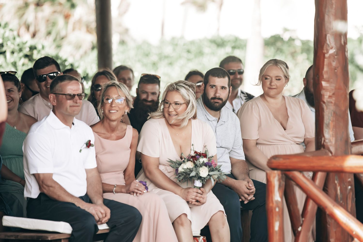 Wedding guests dressed in pink attire seated and watching the ceremony at a tropical outdoor wedding venue.
