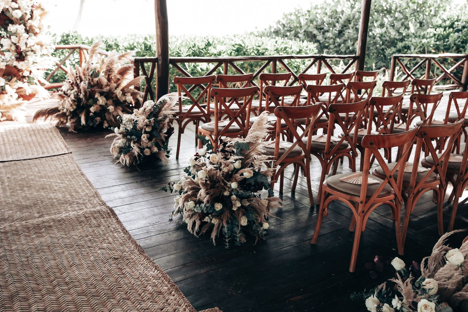 Elegant outdoor wedding ceremony aisle with wooden cross-back chairs and boho floral arrangements.
