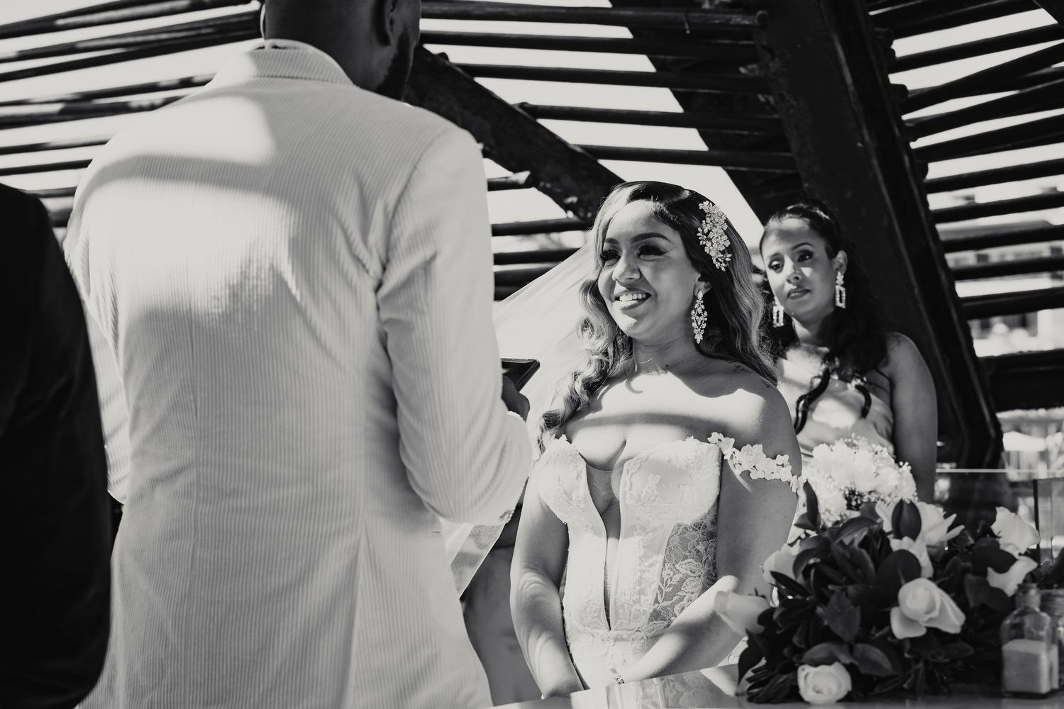 Black and white photo of smiling bride in strapless gown during outdoor wedding ceremony.