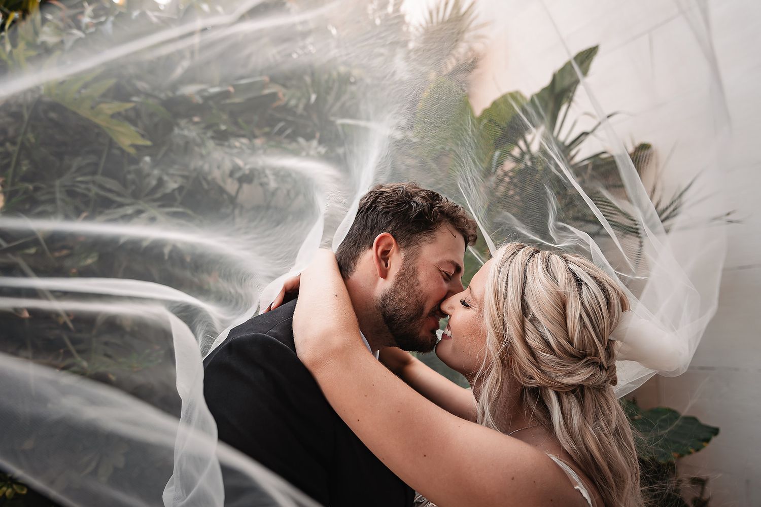 Romantic wedding moment captured through flowing white veil in natural lighting.