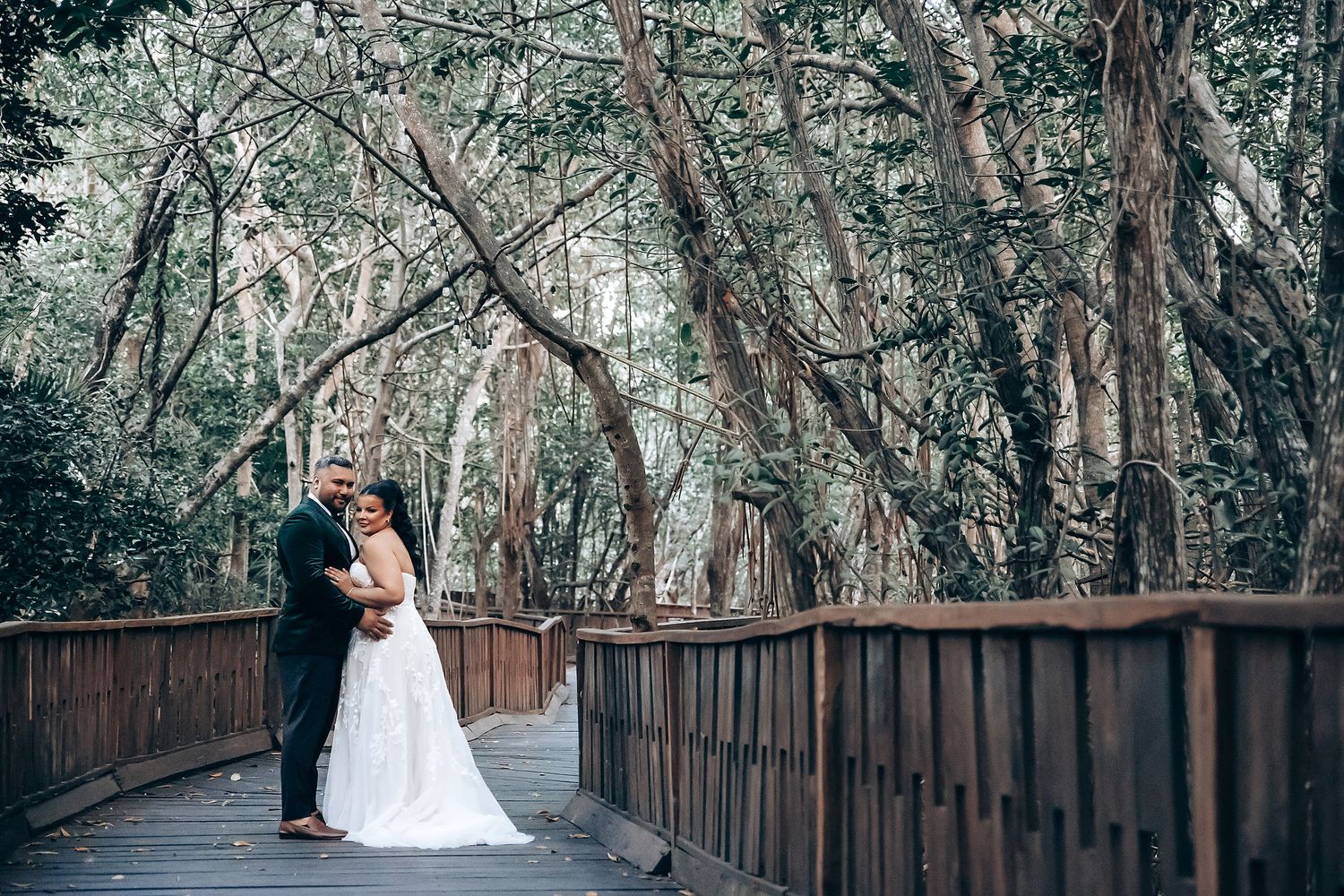 Romantic wedding photo session on wooden boardwalk surrounded by lush forest.