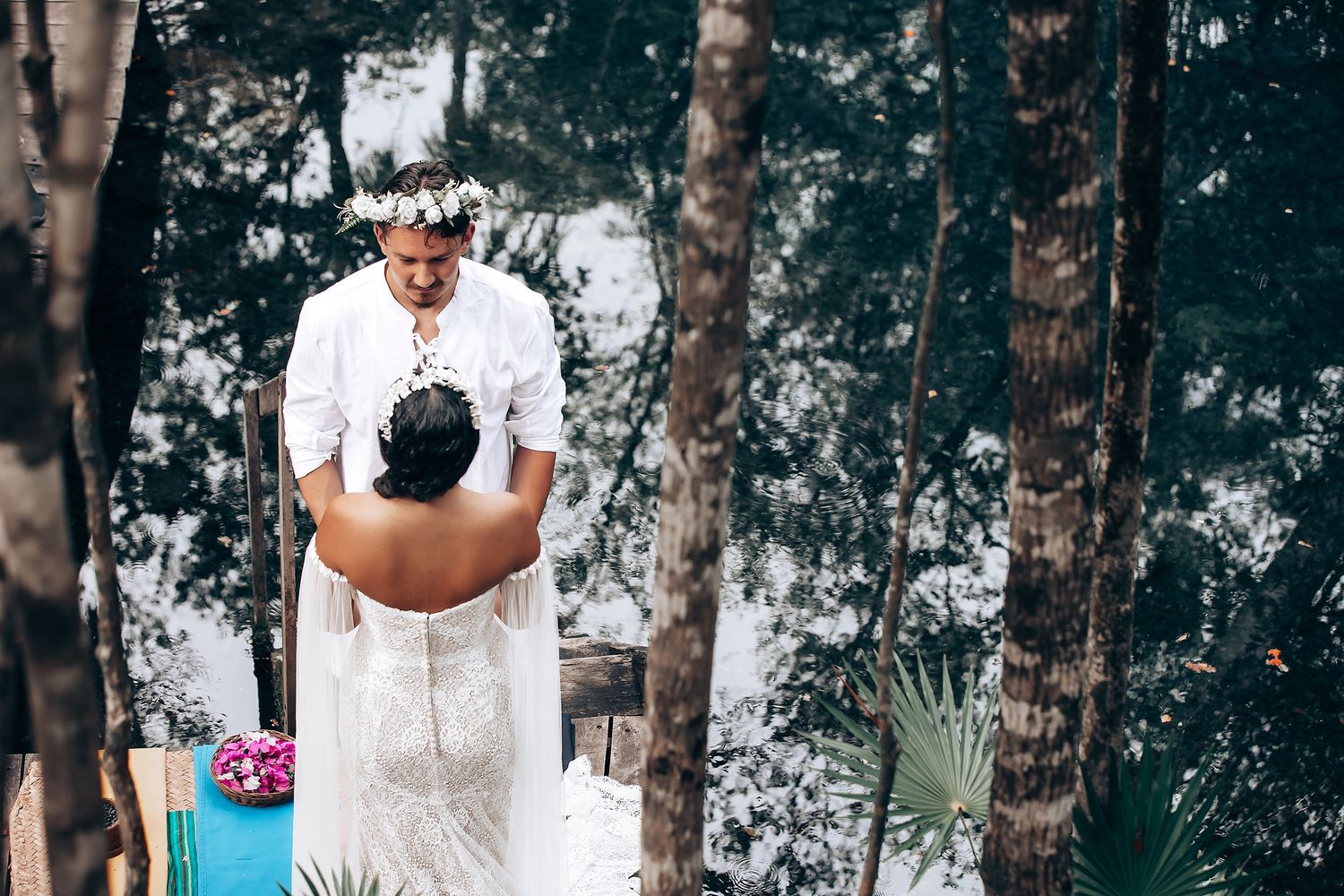 Intimate outdoor wedding scene with guests gathered on a wooden platform against a backdrop of tropical trees.